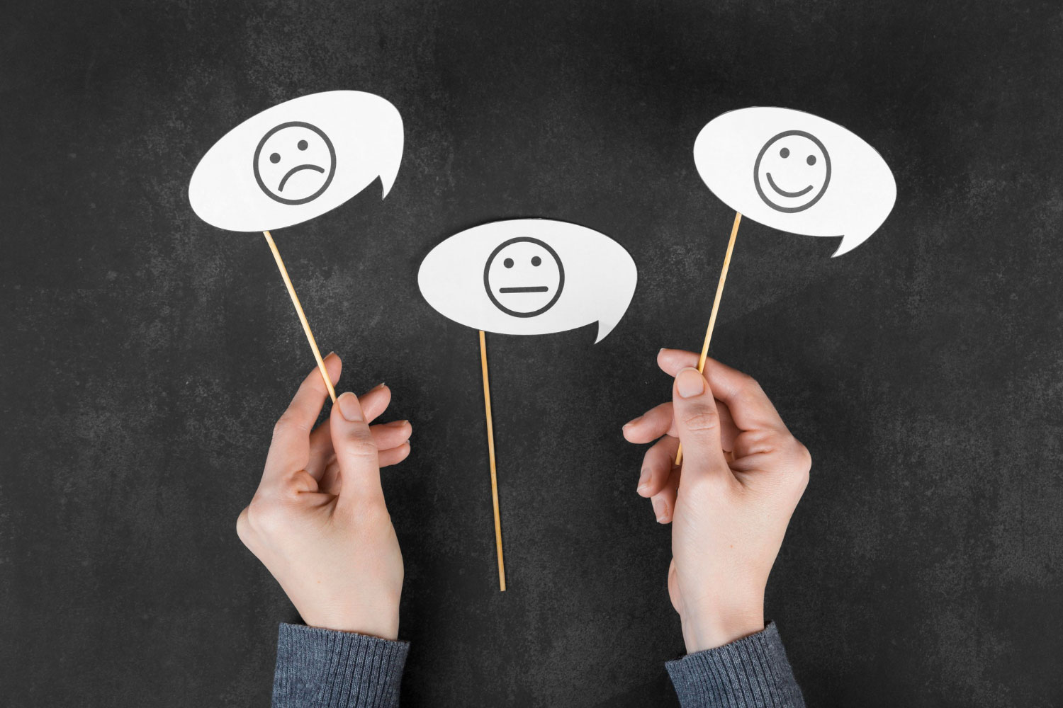 Someone holding up three speech bubbles. One with a sad face, one with an undecided face and one with a happy face. Someone holding up three speech bubbles. One with a sad face, one with an undecided face and one with a happy face.
